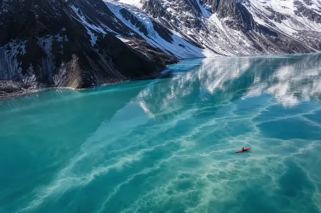 Red kayak crossing a turquoise glacial lake beneath snowy mountains